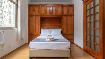 A bedroom with a bed, wooden wardrobe, and a window.