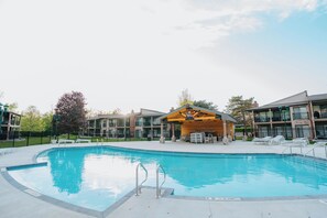 Una piscina con zona de madera para tomar el sol, rodeada de edificios de varios pisos con balcones.