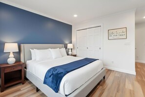 Une chambre à coucher avec un lit, des tables de chevet, un mur bleu, une porte blanche et une citation encadrée accrochée au mur.