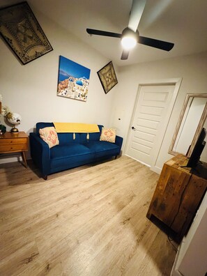 A room with a blue sofa, a wooden side table, a globe, a framed picture, and a ceiling fan. - Theatre Suite in Deep Ellum - Cinema, Skyline & City Vibes (Dallas)