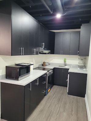 A modern kitchen with dark cabinets, a microwave, an oven, and a sink. - Spacious 2 bedroom Guest suite 9 feet ceiling, 85 inch tv, ping pong kitchen Gym (Oakville)