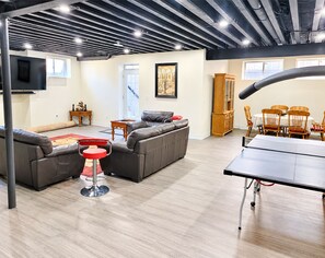 A spacious living area with a sofa, a red bar stool, a ping pong table, and a wooden dining set. - Spacious 2 bedroom Guest suite 9 feet ceiling, 85 inch tv, ping pong kitchen Gym (Oakville)