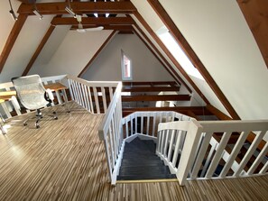 A wooden staircase with white railings leading to a loft area with a desk and office chair.