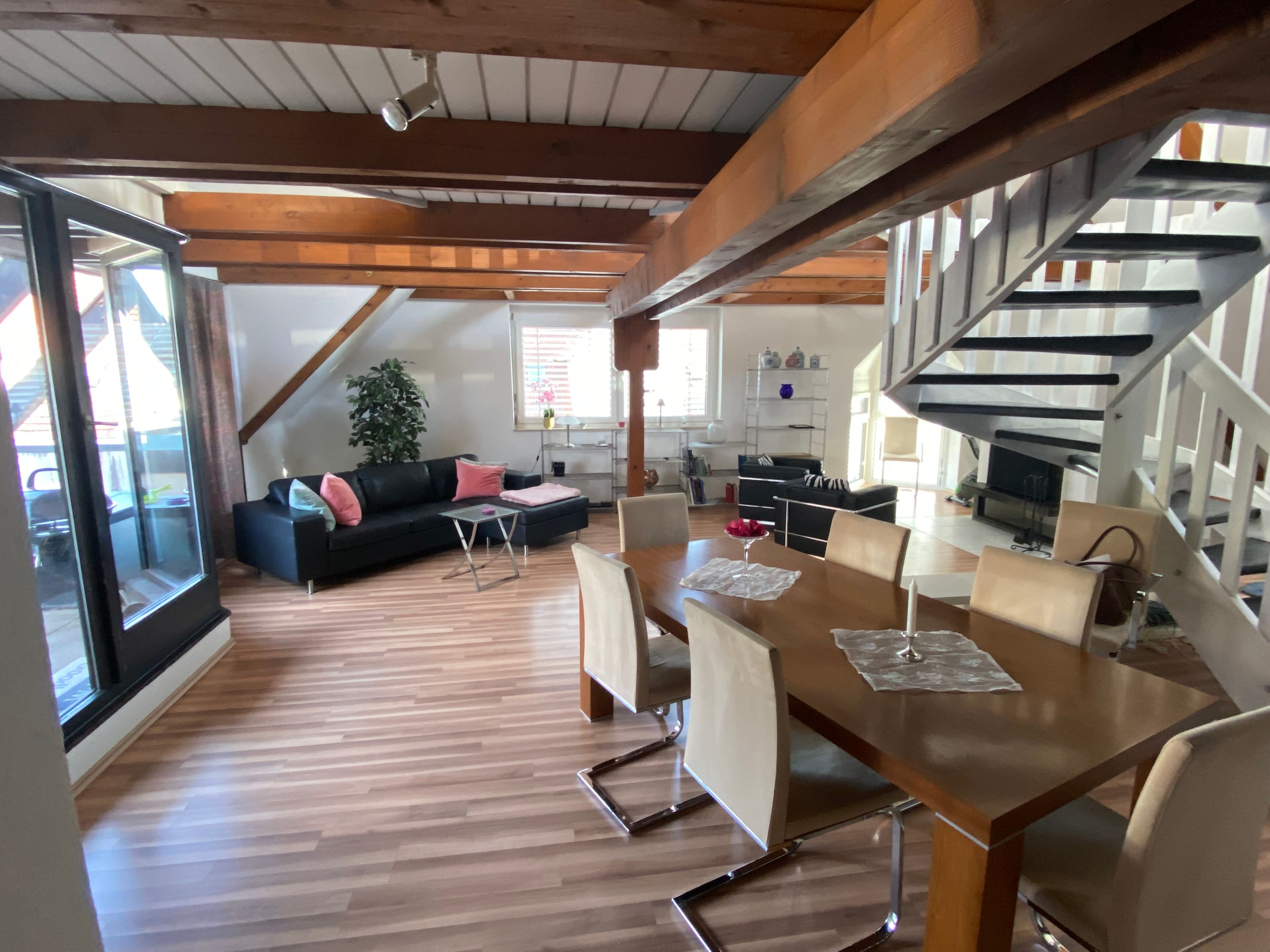 A spacious loft with a dining area, a staircase, and a large window.
