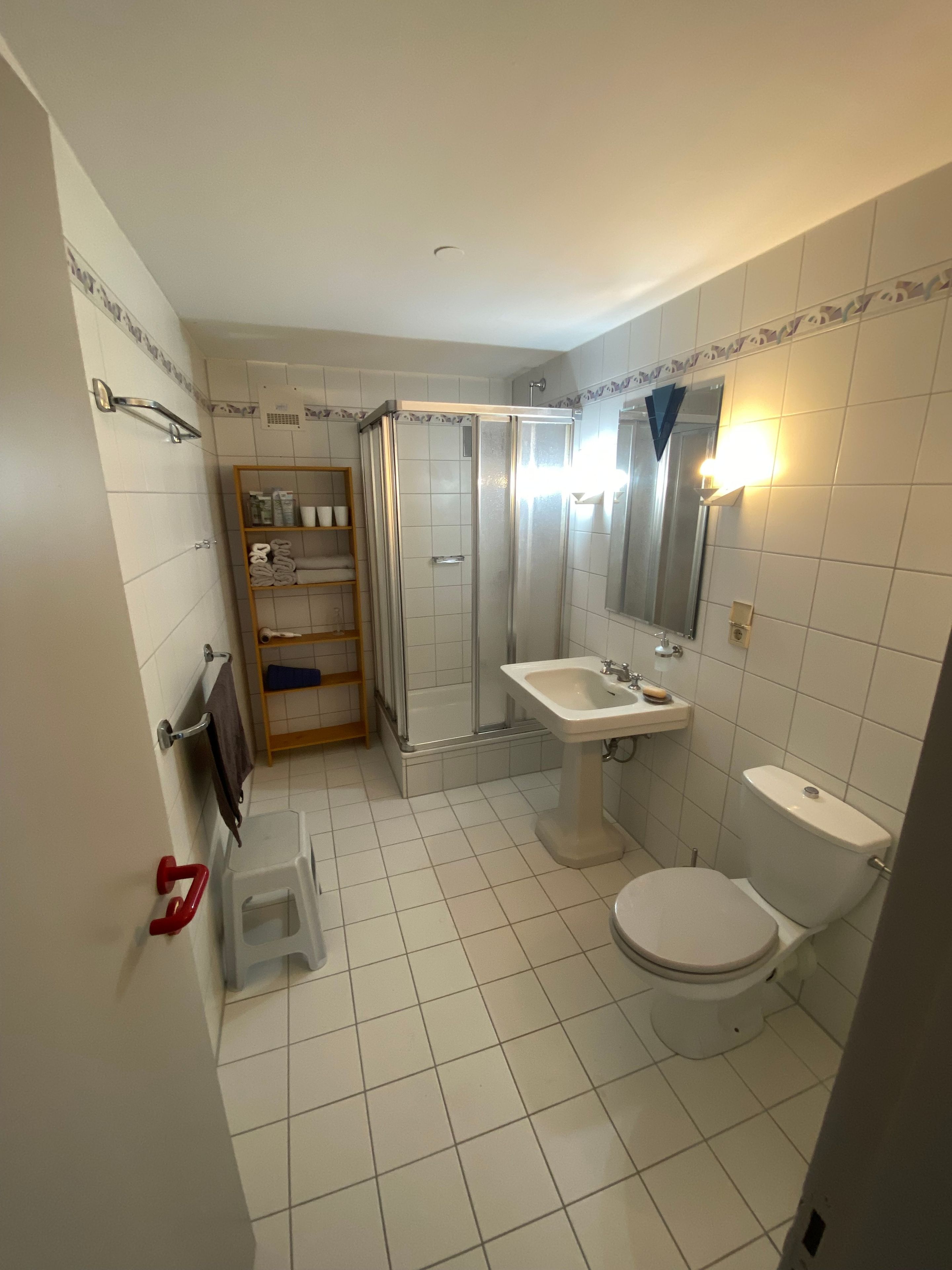 Et badeværelse med brusebad, toilet, håndvask og en hylde med håndklæder.