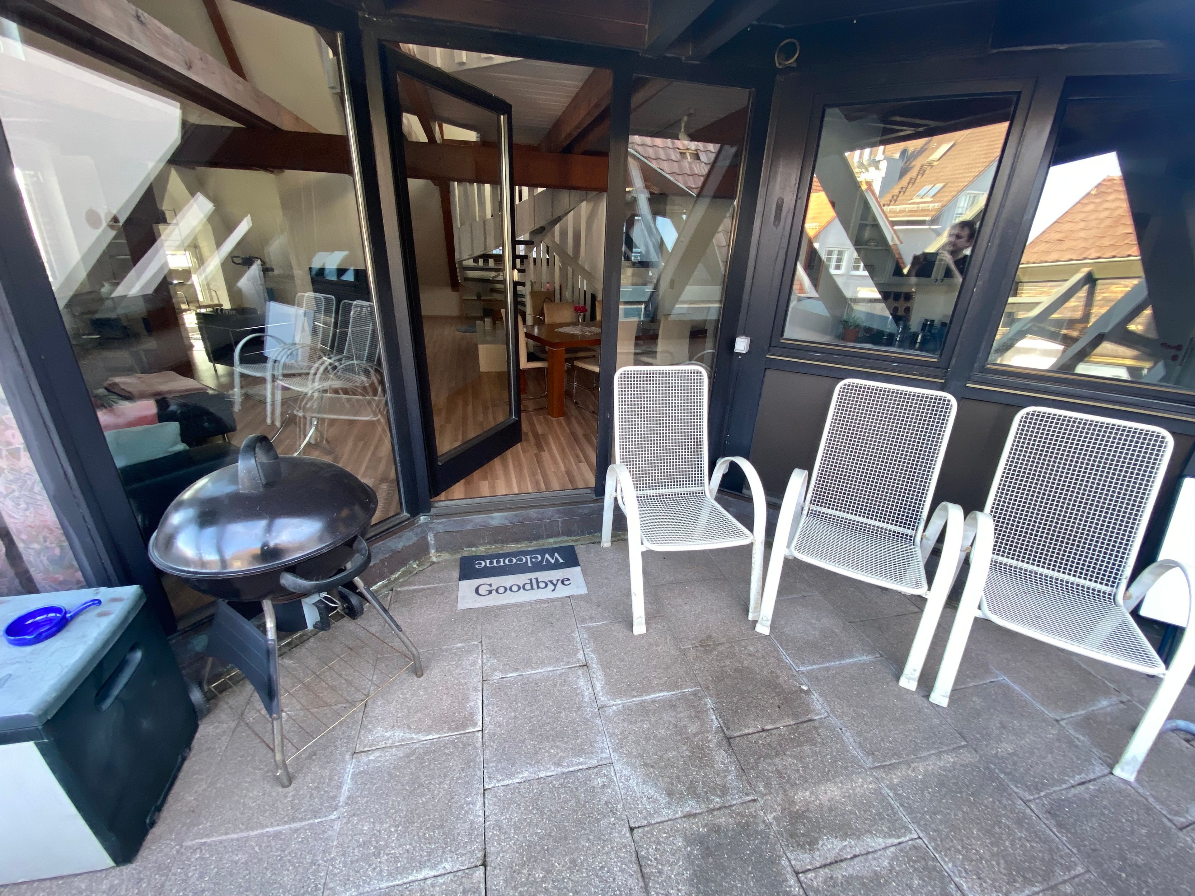 An outdoor seating area with a grill, two metal chairs, and a welcome mat.