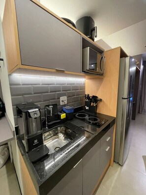 A modern kitchen with a built-in microwave, stainless steel appliances, and a black countertop. - Apartamento em Moema | Varanda e próximo do metrô (São Paulo)
