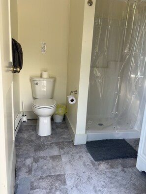 A bathroom with a toilet, a shower enclosure, and a floor mat. - Dream Catcher Cabin #2 · Glamping · Private bath in shared building (Swanton)