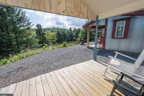 A wooden deck with a gravel path leading to a building with a covered porch. - Dream Catcher Cabin #2 · Glamping · Private bath in shared building (Swanton)