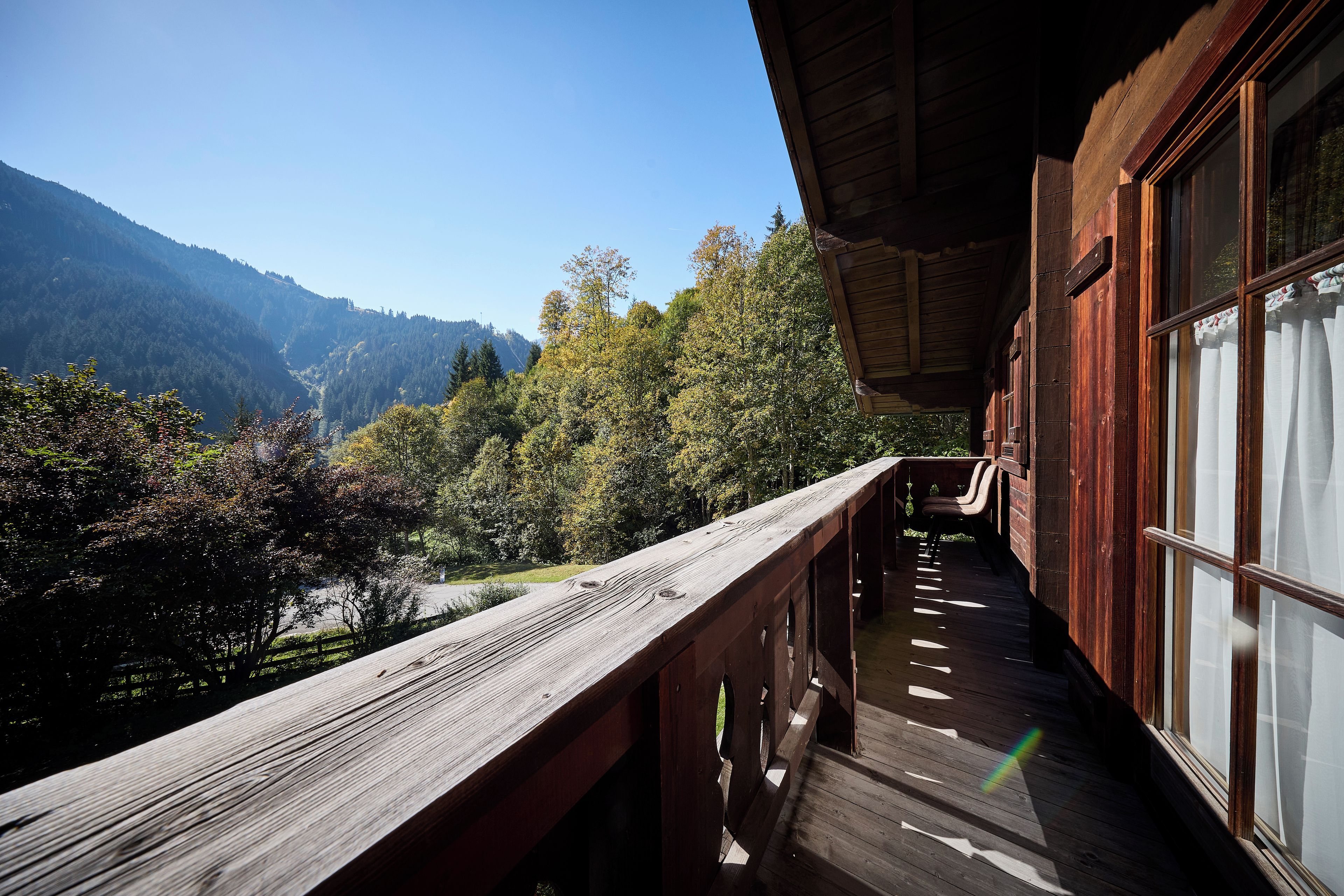 A wooden balcony with a view of a forested valley and mountains.