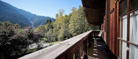 A wooden balcony with a view of a forested valley and mountains.