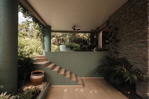 A staircase leading to a covered outdoor area with a ceiling fan, surrounded by greenery and a stone wall. - Eden Escape - Garden Retreat (Pokuase)