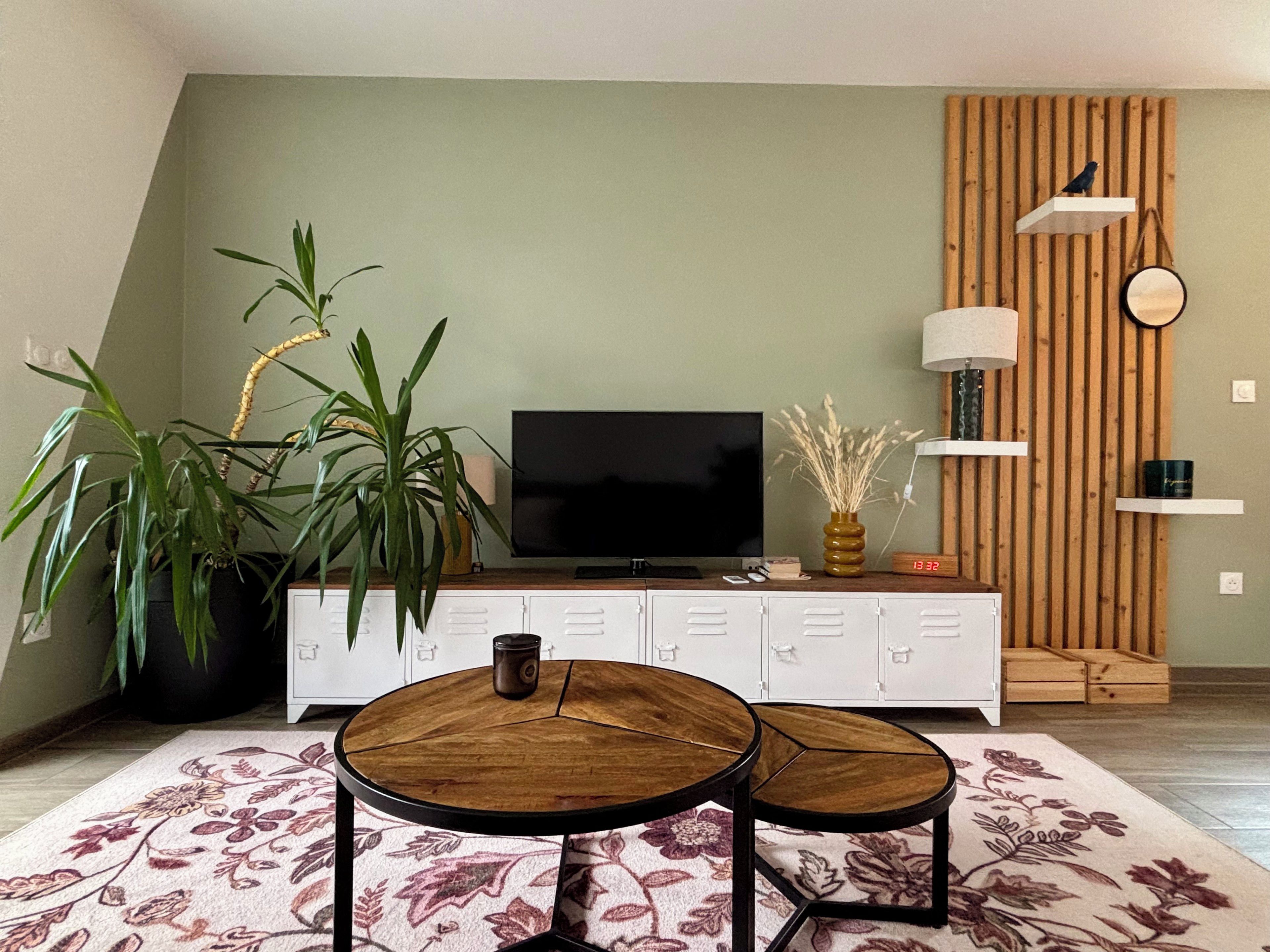 Un salon comprenant un téléviseur à écran plat, un meuble blanc, un buffet en bois, une table basse ronde et une plante en pot.
