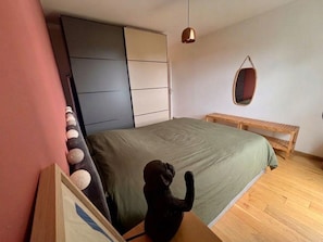 A bedroom with a bed, a wooden bench, a hanging light fixture, and a wardrobe. - Apartment with terrace and garden in Strasbourg (Strasbourg)