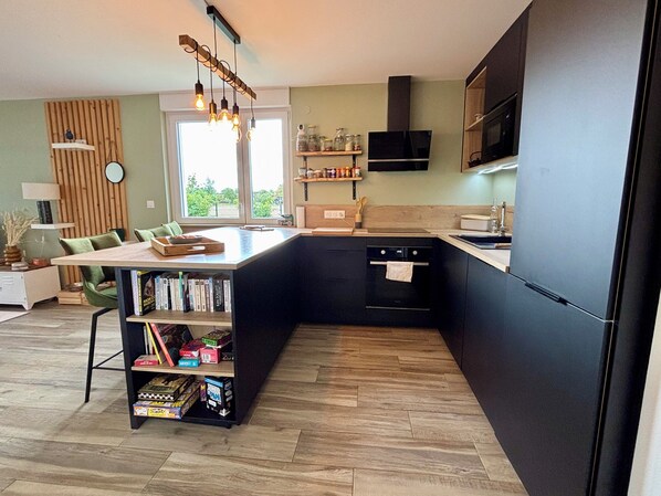 A modern kitchen with a central island, black cabinetry, and a wooden herringbone floor. - Apartment with terrace and garden in Strasbourg (Strasbourg)