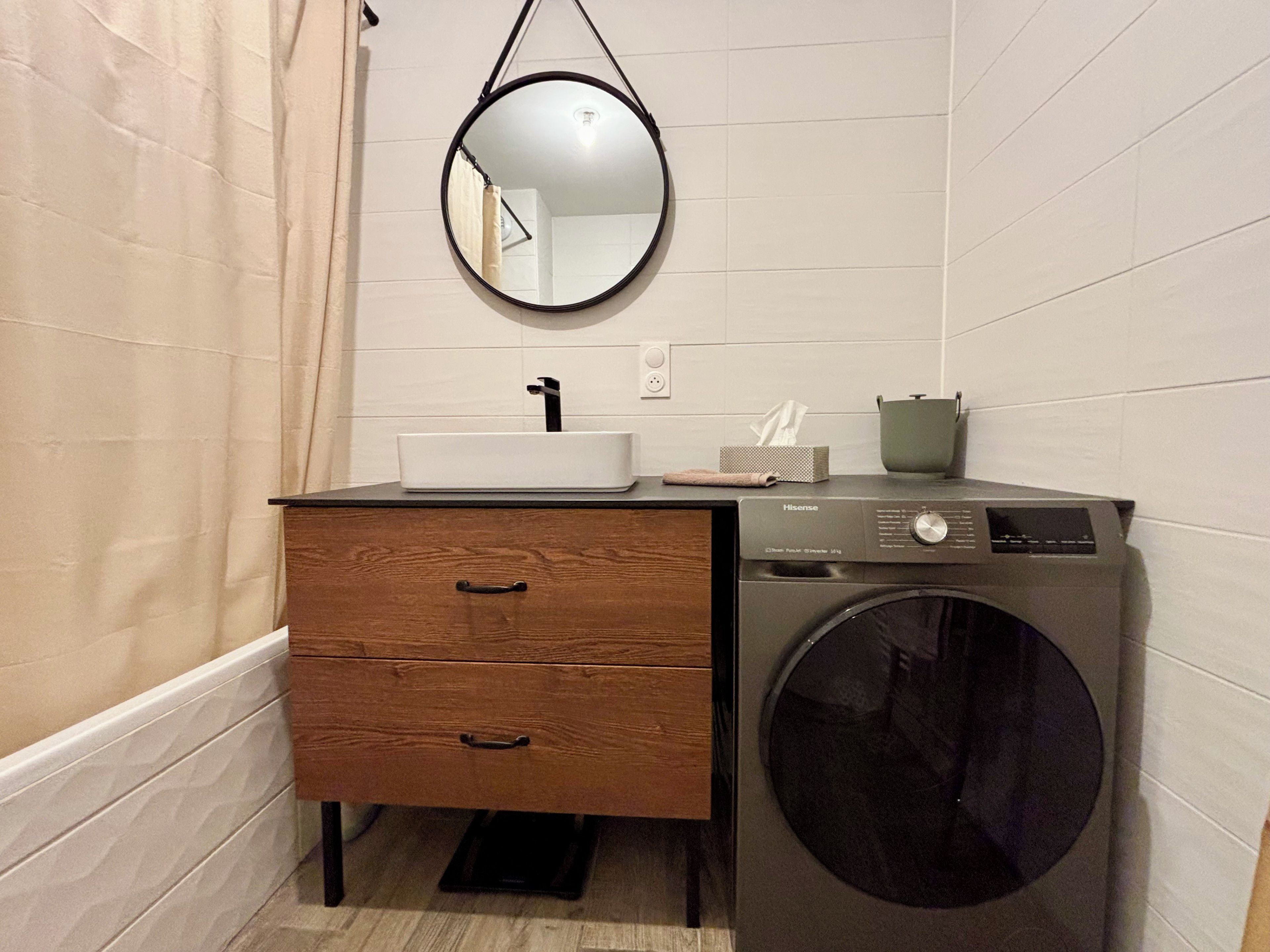 Une petite salle de bain avec un meuble-lavabo en bois, un évier, un miroir, un lave-linge et un porte-serviettes.