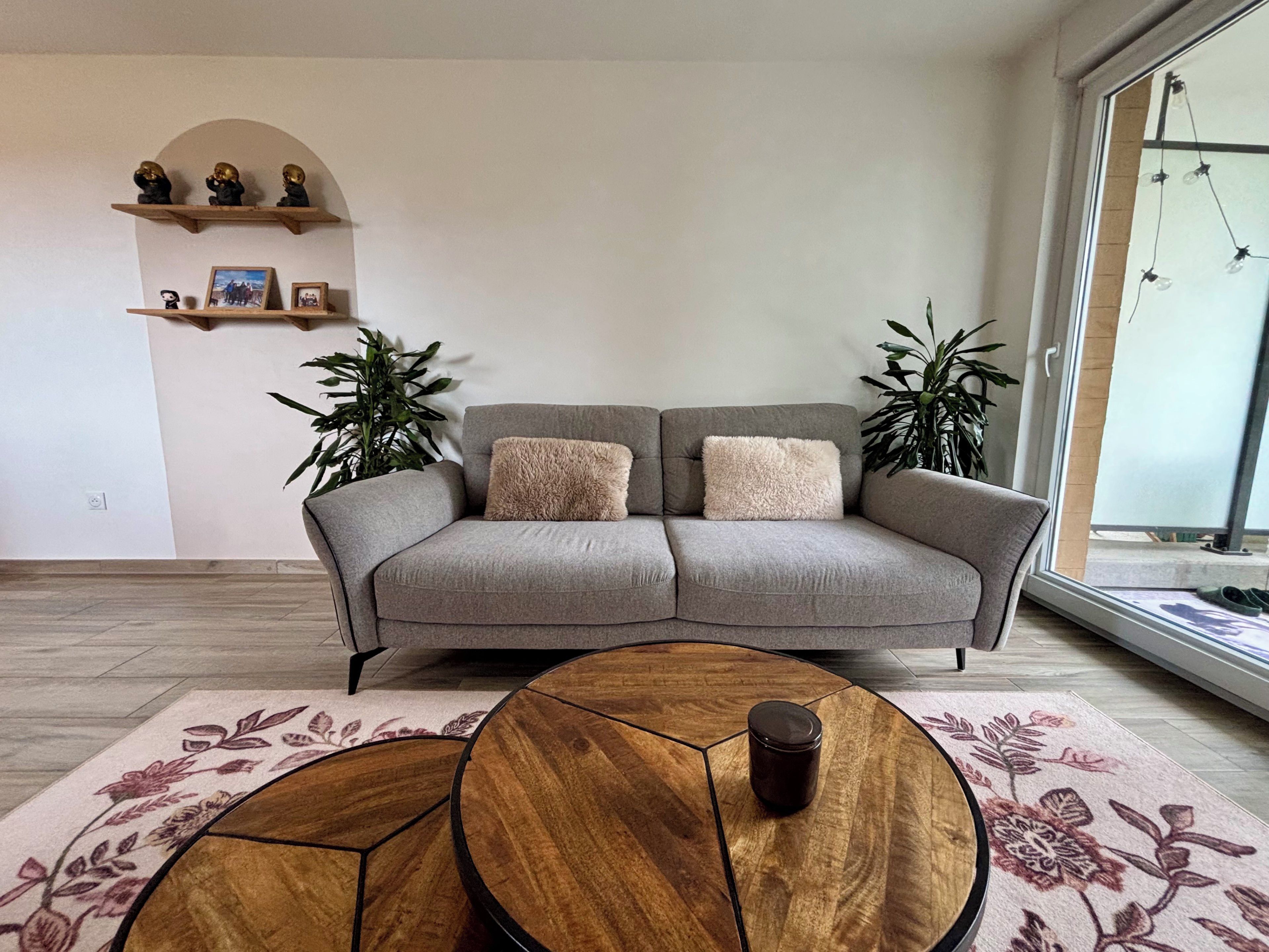 Un salon moderne avec un canapé gris, deux tables d’appoint et une table basse.