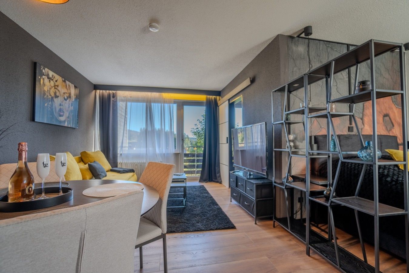 Ein modernes Wohnzimmer mit einer Couch, einem Esstisch und einem Fernseher. Ein Bücherregal und ein Fenster mit Vorhängen sind ebenfalls vorhanden.
