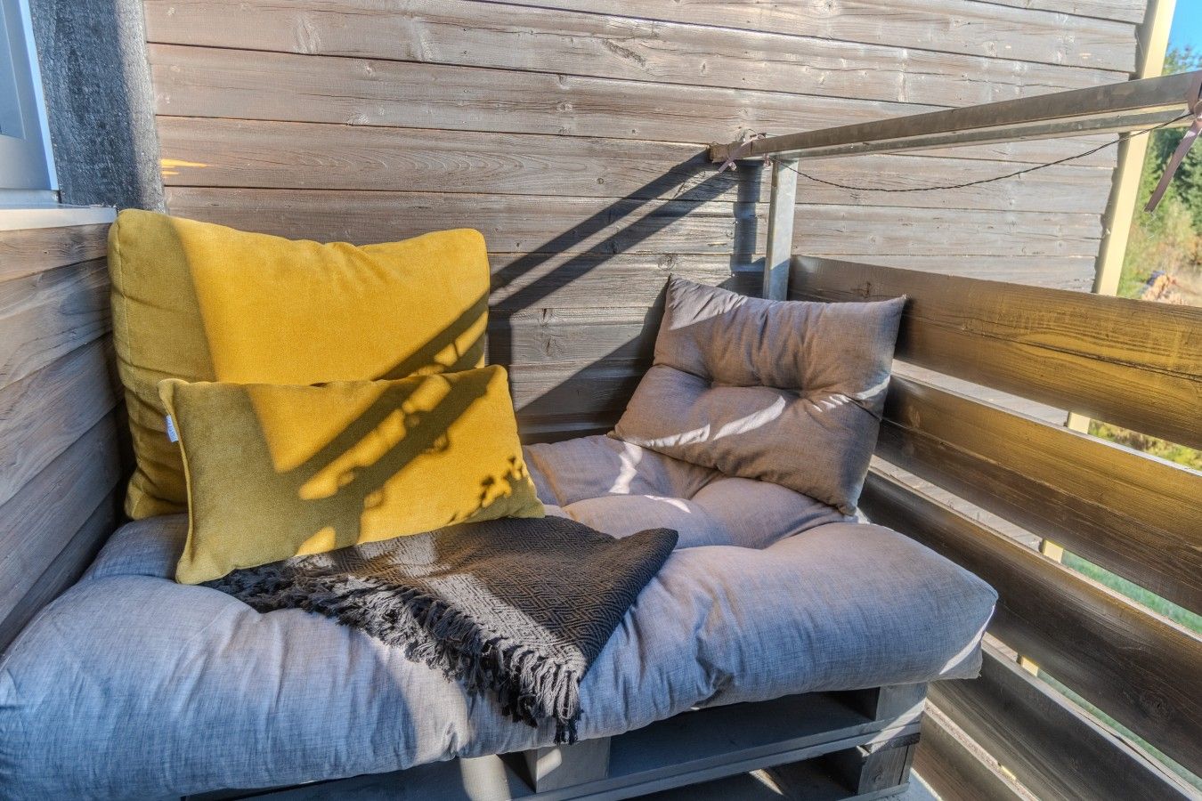 Una terraza de madera con zona de estar acolchada y varios cojines.