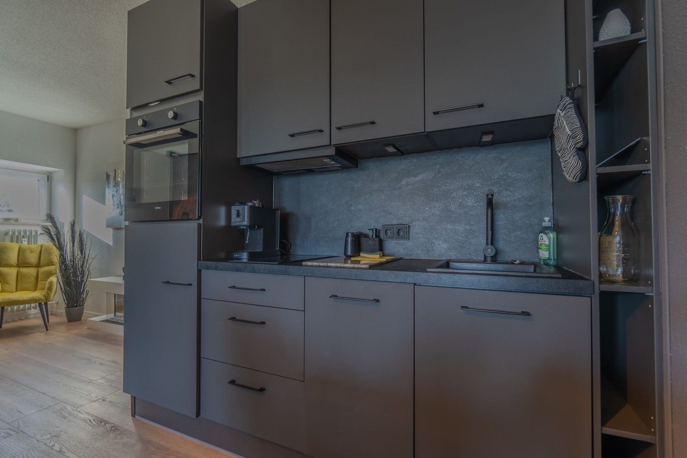 A modern kitchen with dark cabinets, a microwave, a coffee machine, and a sink.