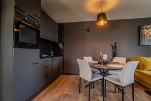 A modern kitchen with dark cabinetry, a dining table with chairs, and a pendant light. - Stylish Apartment in the Bavarian Forest (Haidmühle)