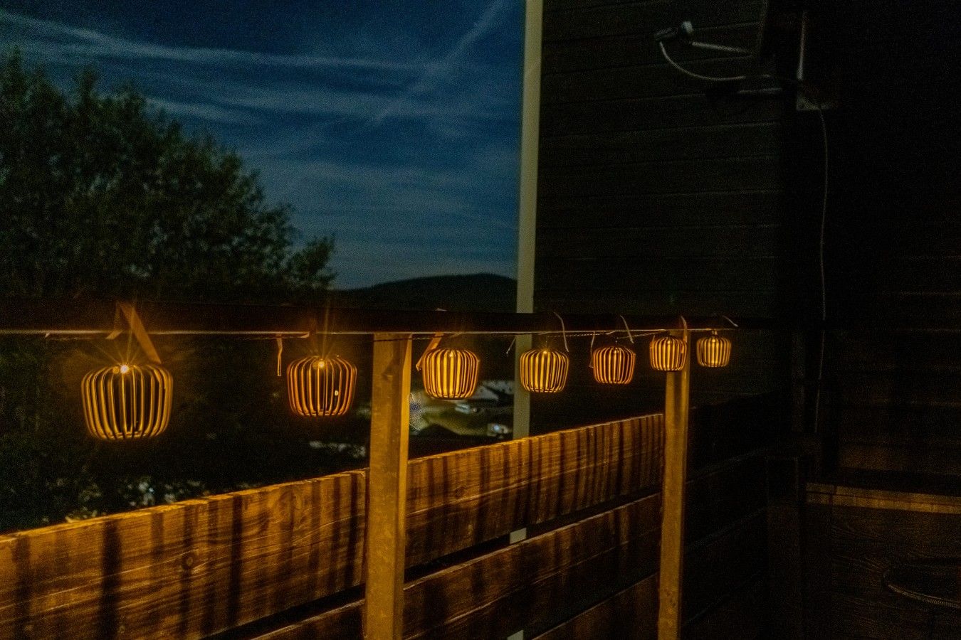 Een houten terras met een leuning, versierd met lichtslingers.
