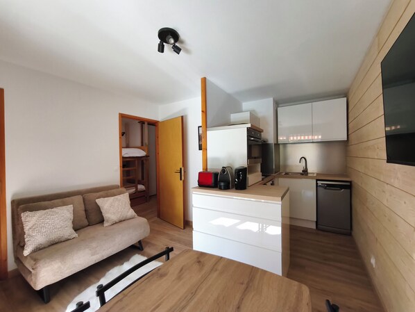 Un espacio habitable compacto con kitchenette, un sofá y piso de madera.