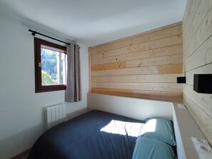Un dormitorio con cama, ventana con cortinas, pared de listones de madera y radiador.