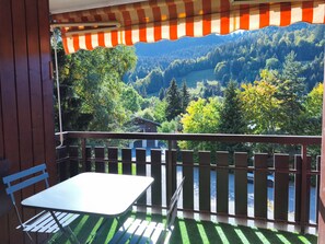 A balcony with a table and chairs, overlooking a forested valley. - Renovated 1-Bedroom Apartment Near the Centre (La Clusaz)