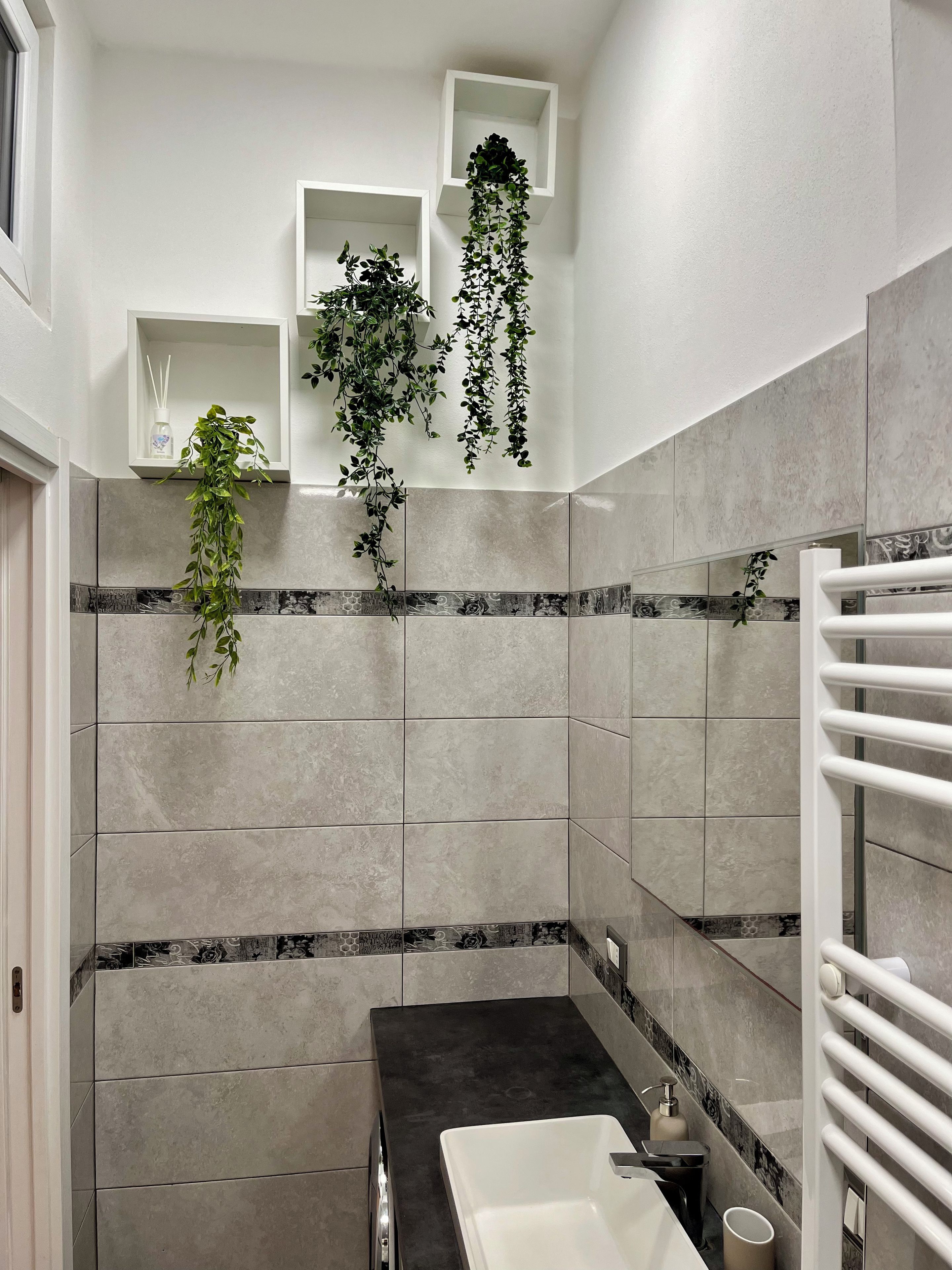 Un bagno moderno con lavabo su un piano nero, mensole bianche e piante pensili.