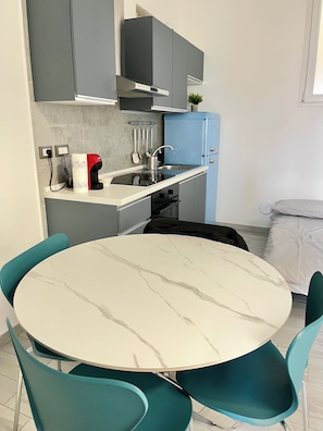 A compact kitchen with grey cabinets, a blue refrigerator, a white countertop, and a round table with teal chairs. - Casa Penelope - Nolo - M1 Rovereto - 15 minutes from the Duomo (Milano)