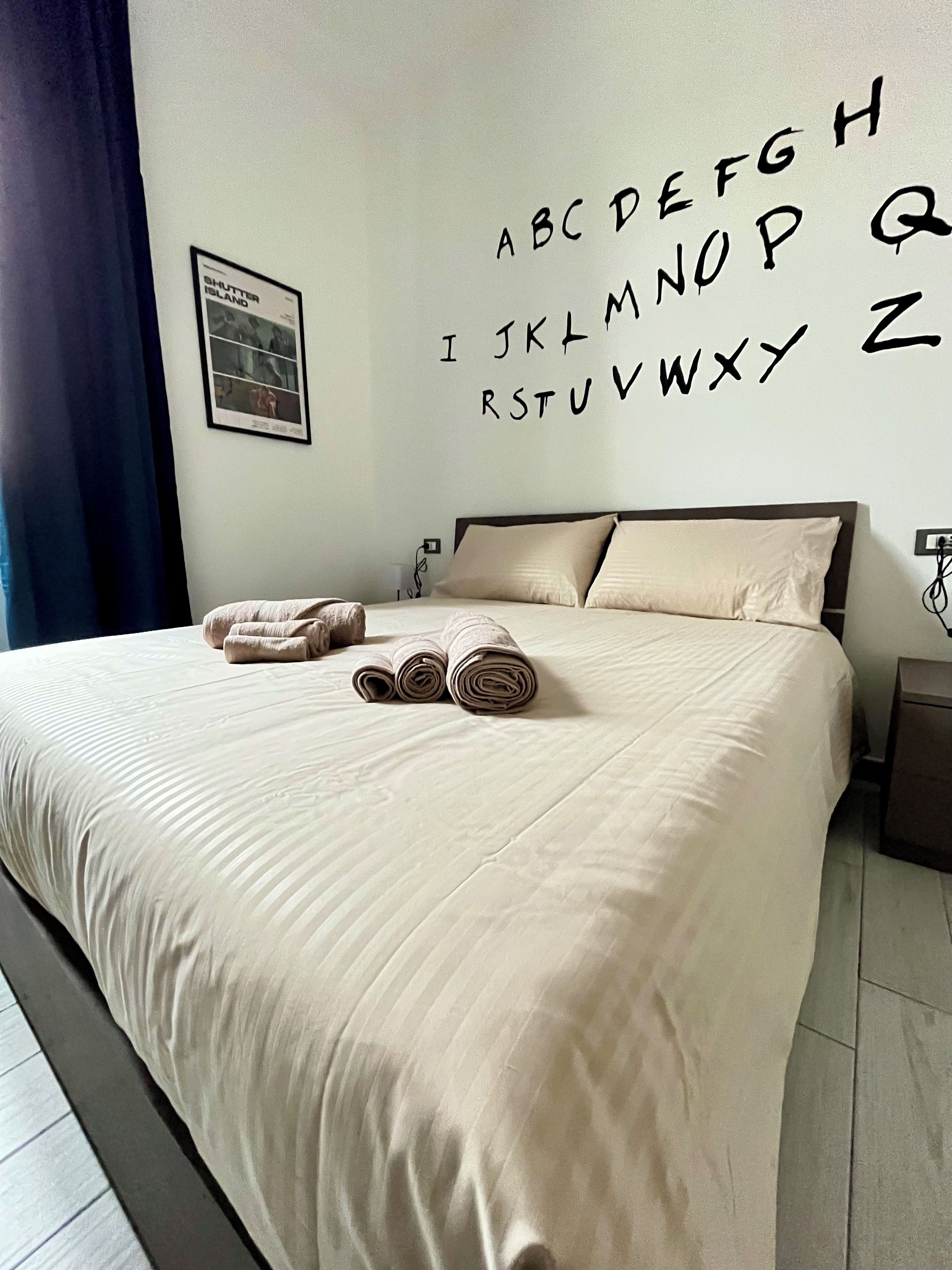 A neatly made bed with rolled towels, a framed picture on the wall, and a wall with large alphabet letters.