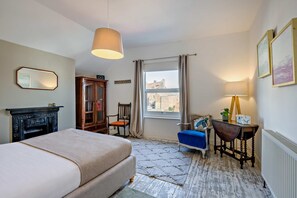 A hotel room with a bed, a desk, a chair, a fireplace, a window with curtains, and a view of buildings outside. - Host & Stay | Indigo Snug (Cromer)