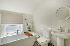 A bathroom with a bathtub, toilet, sink, and a window with frosted glass. - Host & Stay | Indigo Snug (Cromer)