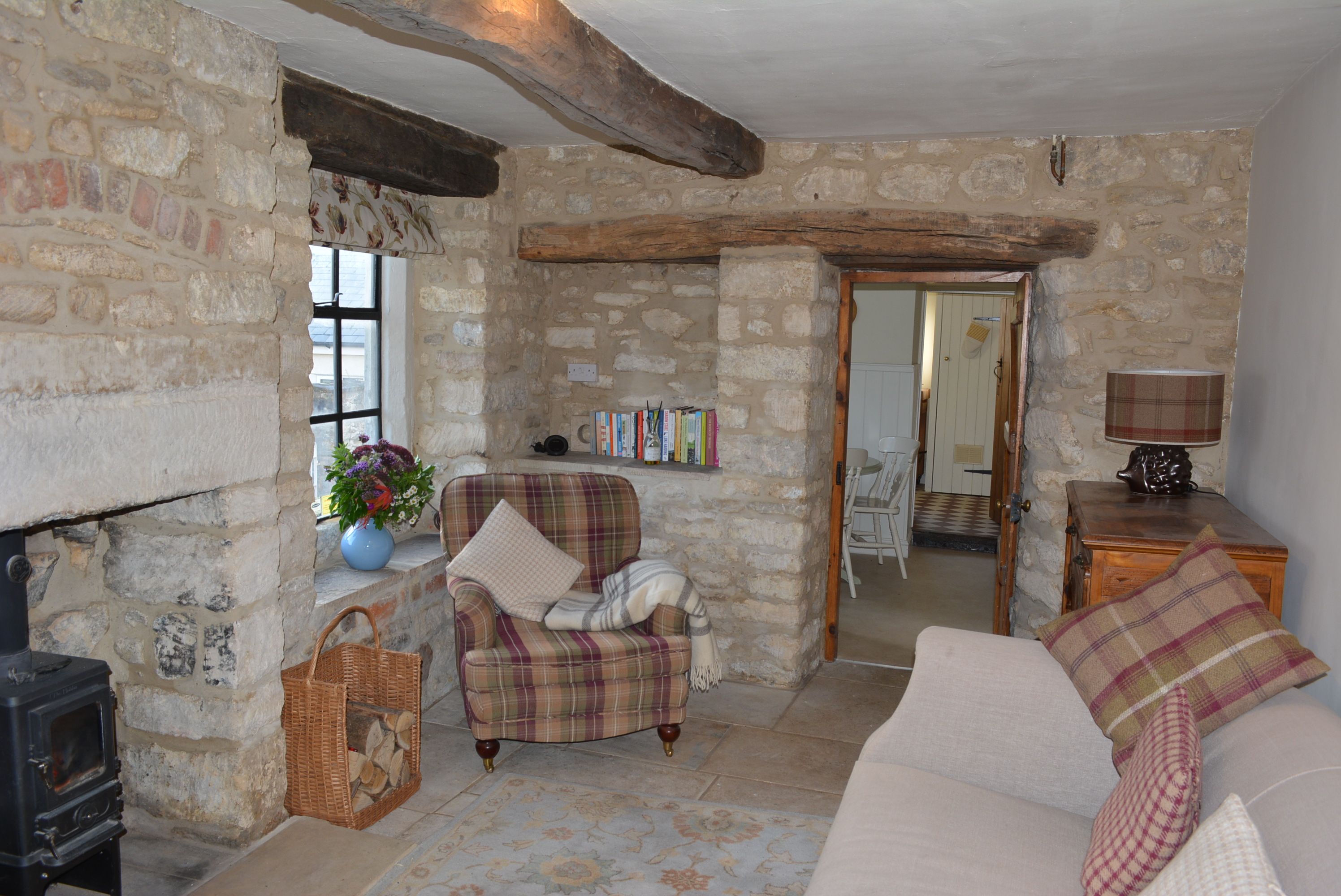 A rustic living room with exposed stone walls, a fireplace, a plaid armchair, a sofa, and a bookshelf.