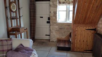 A rustic room with a wooden chair, a white door, a window with floral curtains, and a radiator.