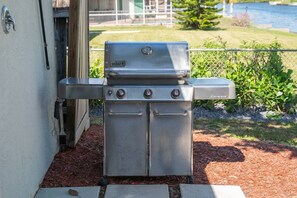 A Weber Genesis portable gas grill with four burners, positioned outdoors near a building. - Amazing Canal Home, Heated Pool, Spa & Fishing (Cape Coral)