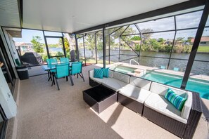 A covered outdoor area with a pool, seating, and a view of a body of water. - Amazing Canal Home, Heated Pool, Spa & Fishing (Cape Coral)