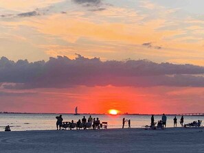 A beach scene with people relaxing and a sunset in the background. - Cozy Coastal Charmer with heated pool and beach gear (Cape Coral)