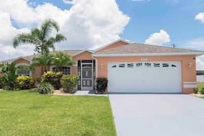 A single-story house with a garage, a well-maintained lawn, and a palm tree. - Cozy Coastal Charmer with heated pool and beach gear (Cape Coral)