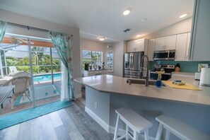 Cozinha moderna com uma ilha grande, eletrodomésticos de aço inoxidável e vista para uma área de piscina.