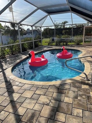 A swimming pool with two pink swan floats, surrounded by a covered area with a tiled floor. - Heated pool, fast WiFi, ideal location. Perfect for families (Cape Coral)