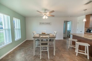 A dining area with a table and chairs, a ceiling fan, and a kitchen area with a counter and stools. - Heated pool, fast WiFi, ideal location. Perfect for families (Cape Coral)