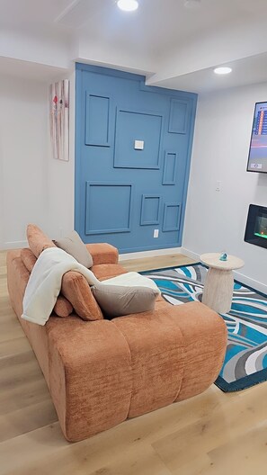 A living room with a blue accent wall, a sofa, a small table, and a flat-screen TV mounted on the wall. - Modern, Clean and cozy suite (Edmonton)