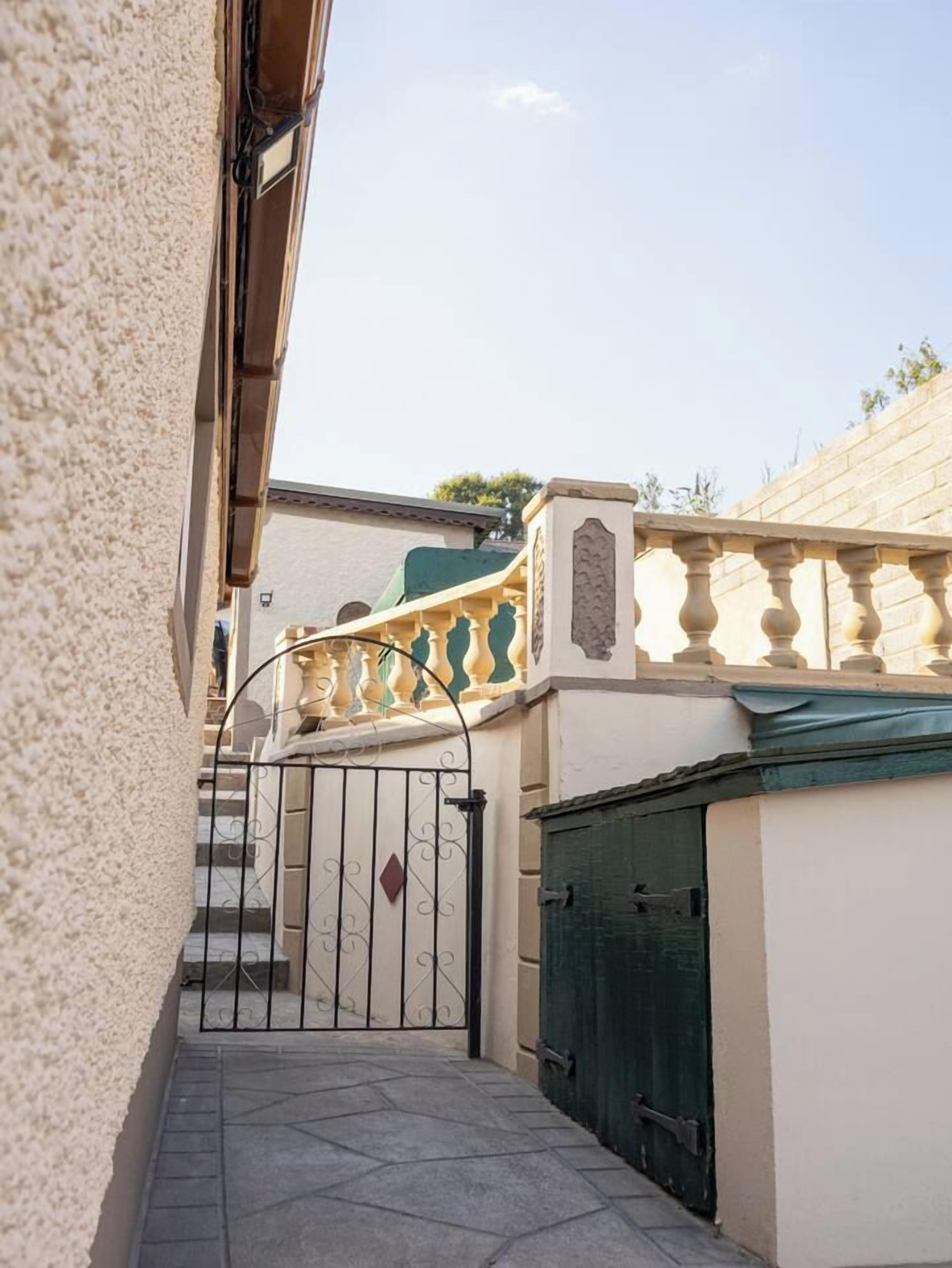 A narrow alleyway with a gated entrance, a tiled pathway, and a building with a green door.