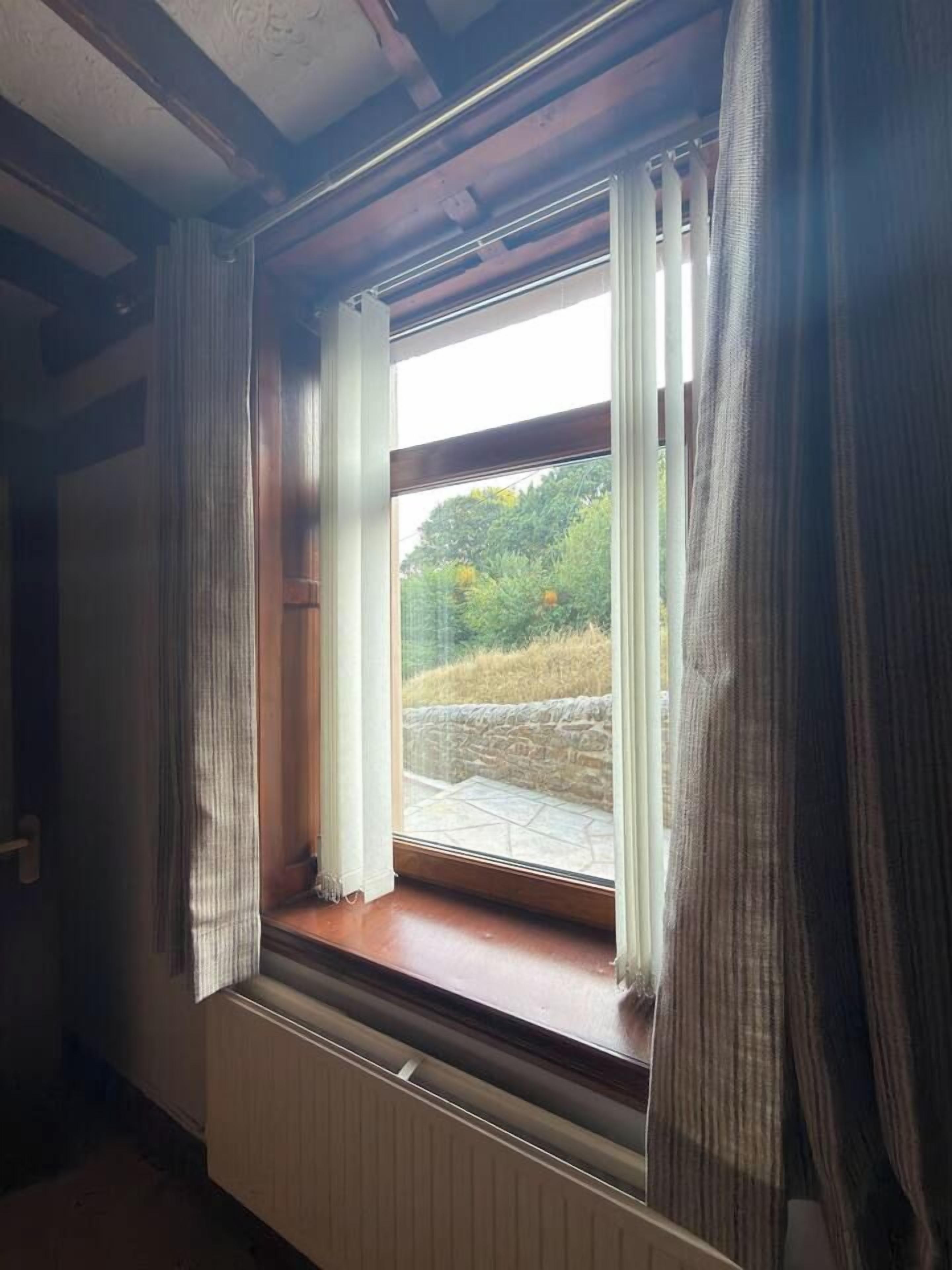Ein Zimmer mit Fensterblick auf eine Steinmauer und Grünpflanzen.