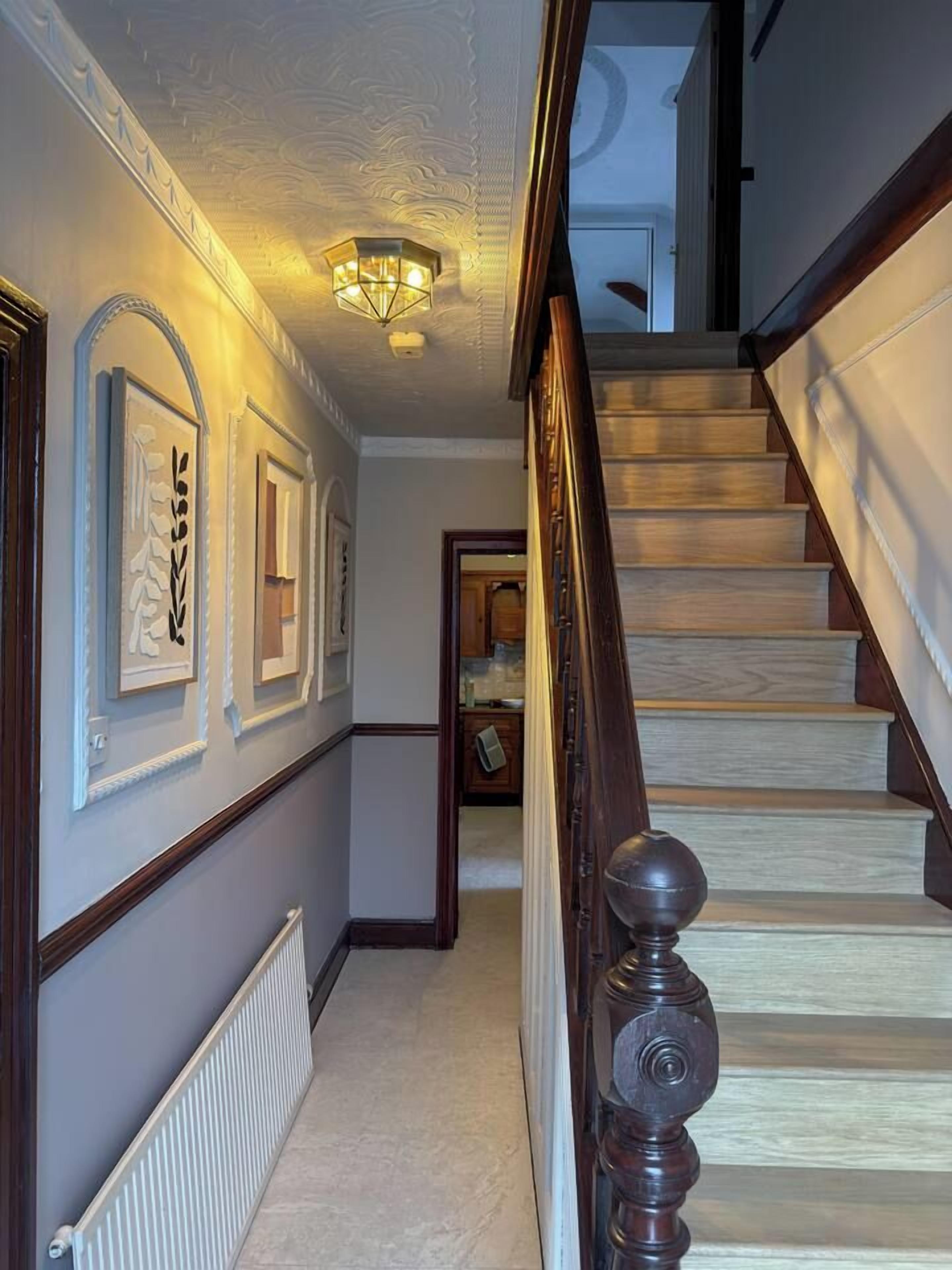 A hallway with a wooden staircase, a radiator, and framed artwork on the walls.