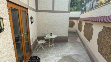A narrow outdoor patio with a table and chairs, a door with glass panels, and a small decorative rug.