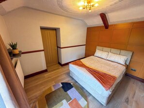 Une chambre à coucher avec un lit, une porte en bois, une petite table avec une plante et un tapis à motifs.