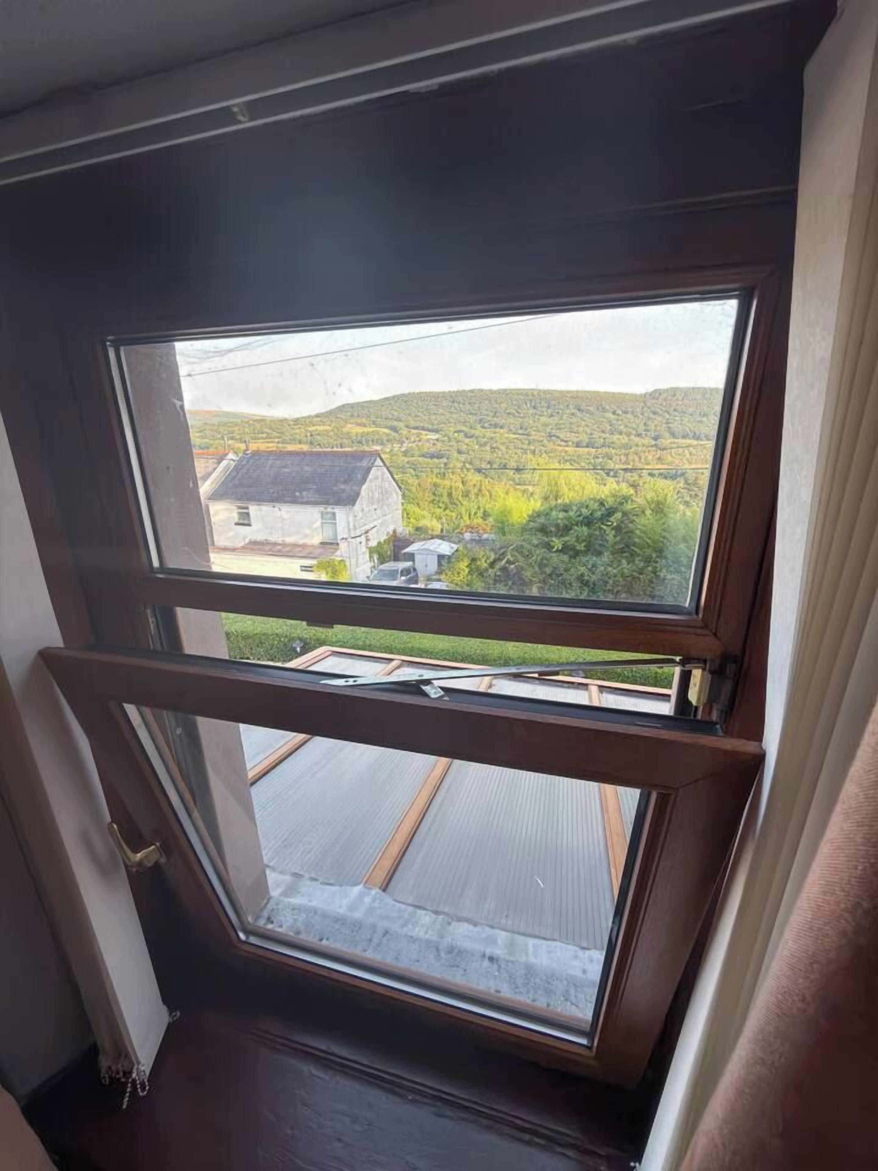 Une fenêtre donnant sur une maison et un paysage verdoyant.